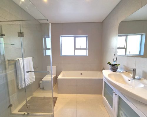 Luxury Beach Holiday Accommodation in Sunset Beach, Cape Town Modern luxury bathroom at The Sunset Beach House featuring a walk-in shower, soaking bath, elegant vanity and premium finishes in Sunset Beach, Cape Town.