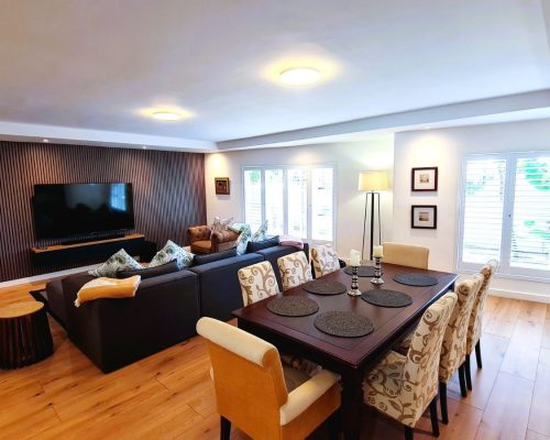 Luxury Beach Holiday Accommodation in Sunset Beach, Cape Town Open plan dining and living area with wooden cladding feature wall and white American shutter blinds at sunset beach house Cape Town