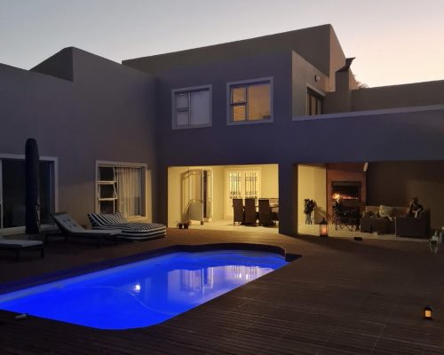 Luxury Beach Holiday Accommodation in Sunset Beach, Cape Town Luxury pool and wooden deck at dusk with ambient lighting at sunset beach house Cape Town holiday accommodation